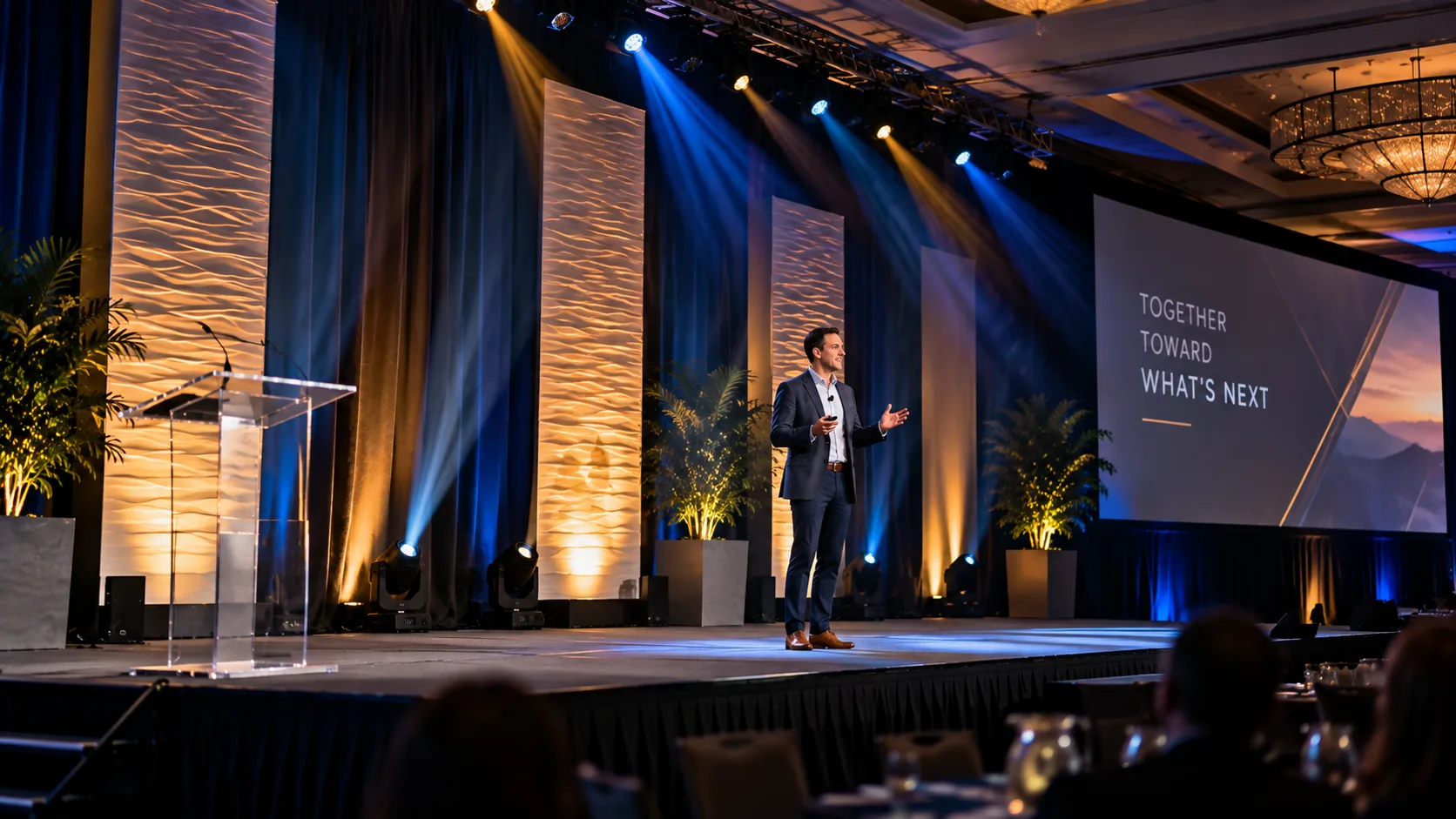 Stage lighting balancing the presenter, scenic backdrop and screens